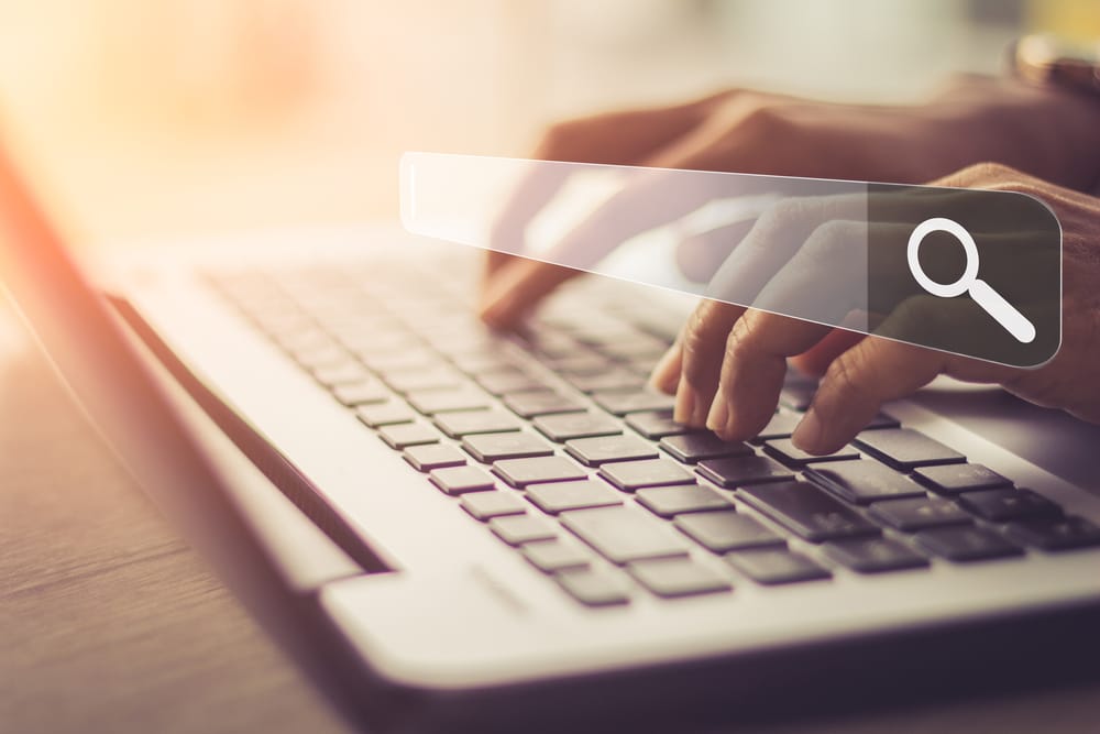 Person typing on a laptop with a Google search bar superimposed over the image