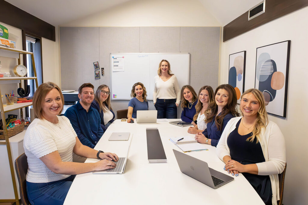 The members of Arrow Marketing meet at a white boardroom table and look at the camera.
